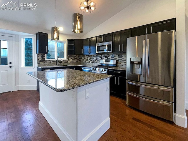 kitchen with appliances with stainless steel finishes, hanging light fixtures, a center island, vaulted ceiling, and dark stone counters