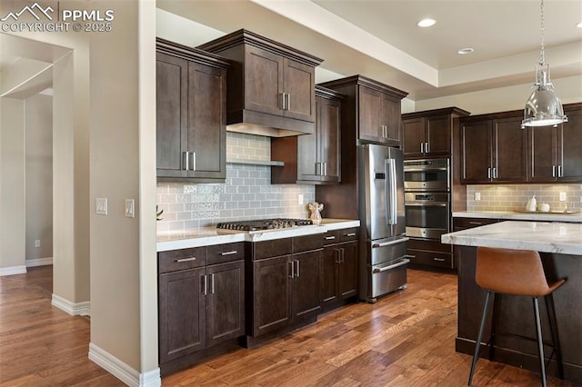 kitchen with dark wood-type flooring, a breakfast bar, dark brown cabinets, appliances with stainless steel finishes, and decorative backsplash