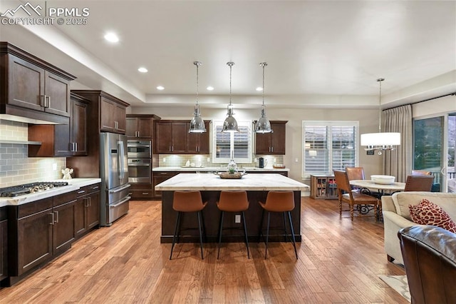 kitchen featuring a breakfast bar, a center island, dark brown cabinets, hanging light fixtures, and appliances with stainless steel finishes