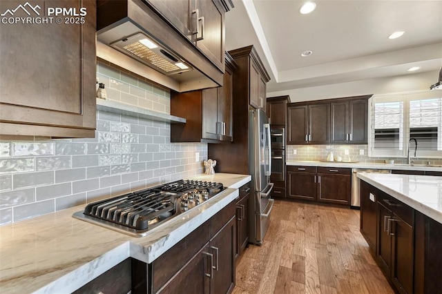 kitchen with sink, stainless steel gas cooktop, dark brown cabinetry, light wood-type flooring, and wall chimney exhaust hood