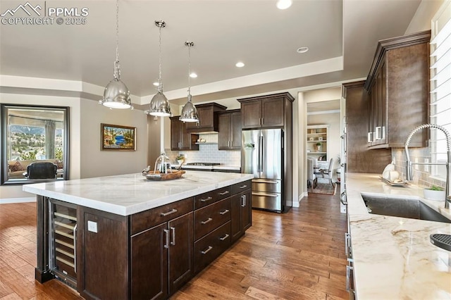 kitchen with sink, hanging light fixtures, stainless steel appliances, light stone countertops, and a large island with sink