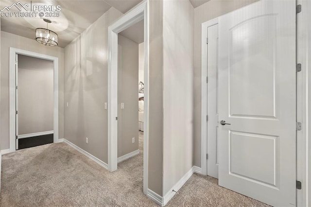 hall with light carpet and an inviting chandelier