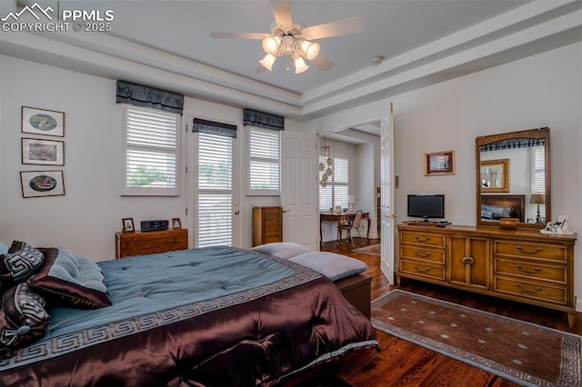 bedroom with ceiling fan, access to exterior, dark hardwood / wood-style flooring, and a tray ceiling