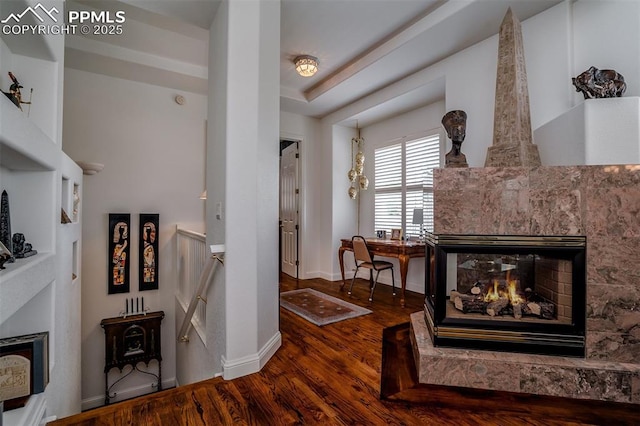 living area with a multi sided fireplace, wood-type flooring, and a raised ceiling