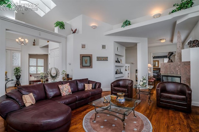 living room with an inviting chandelier, a skylight, built in features, and dark hardwood / wood-style floors