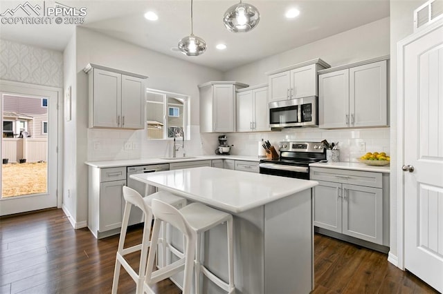 kitchen featuring appliances with stainless steel finishes, pendant lighting, sink, gray cabinetry, and a center island