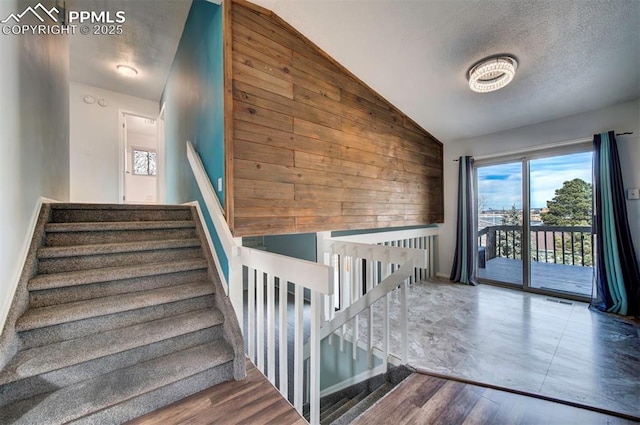 staircase featuring a textured ceiling, vaulted ceiling, wooden walls, and wood-type flooring