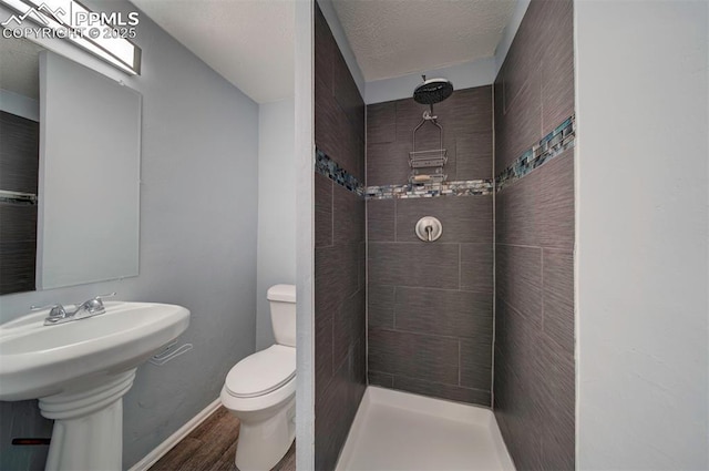 bathroom with wood-type flooring, a tile shower, a textured ceiling, and toilet