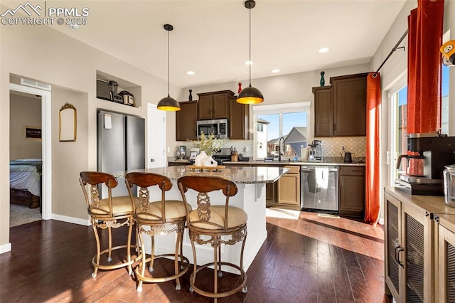 kitchen featuring dark wood-type flooring, a kitchen island, pendant lighting, stainless steel appliances, and light stone countertops