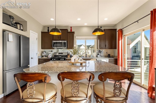 kitchen featuring pendant lighting, dark brown cabinets, stainless steel appliances, light stone countertops, and a kitchen island