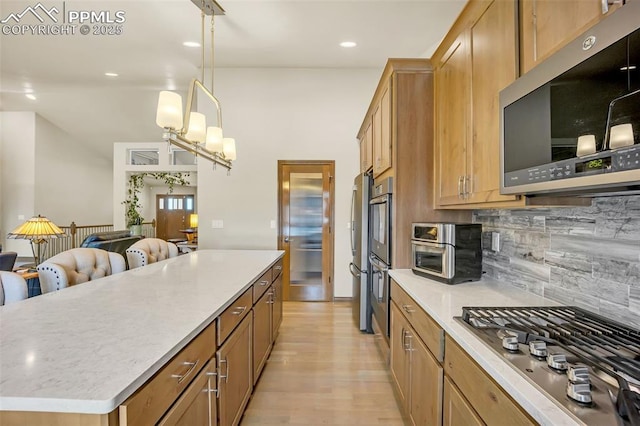 kitchen with pendant lighting, decorative backsplash, a center island, stainless steel appliances, and light wood-type flooring