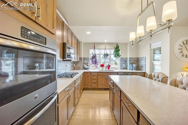 kitchen with pendant lighting, sink, decorative backsplash, light hardwood / wood-style floors, and stainless steel appliances