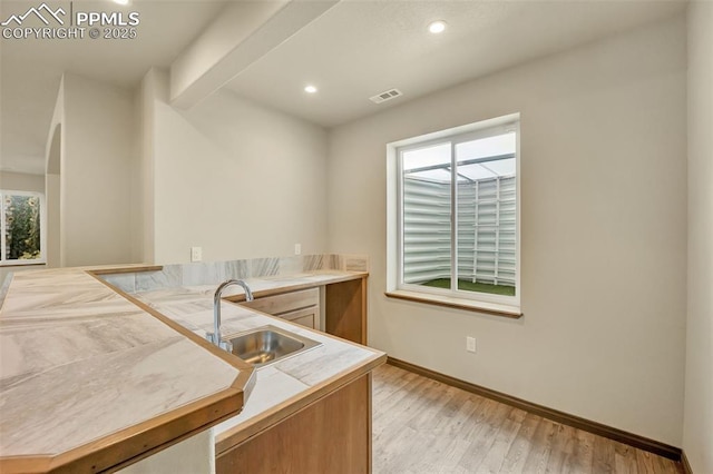 kitchen featuring a healthy amount of sunlight, beam ceiling, light hardwood / wood-style floors, and sink