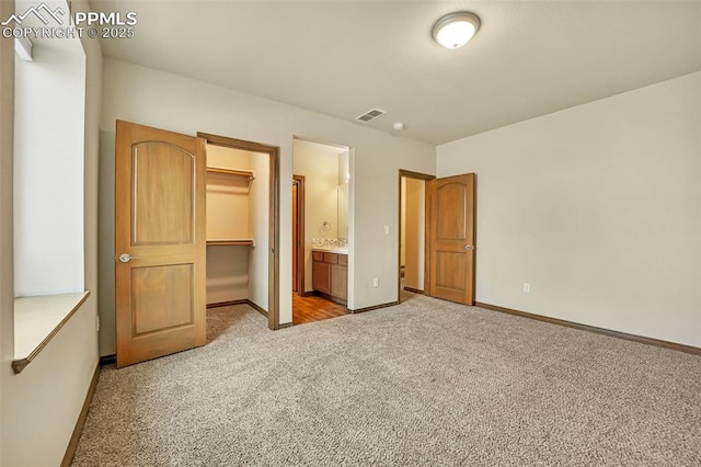 unfurnished bedroom with connected bathroom, a walk in closet, light colored carpet, and a closet