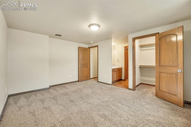 unfurnished bedroom with a closet, ensuite bathroom, a spacious closet, and light carpet