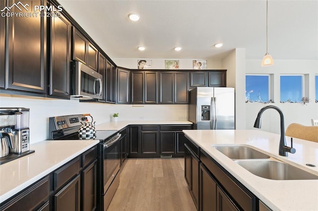 kitchen featuring appliances with stainless steel finishes, pendant lighting, sink, dark brown cabinetry, and light hardwood / wood-style flooring