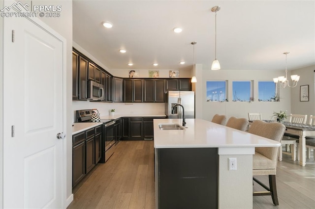 kitchen with sink, a breakfast bar, appliances with stainless steel finishes, an island with sink, and decorative light fixtures