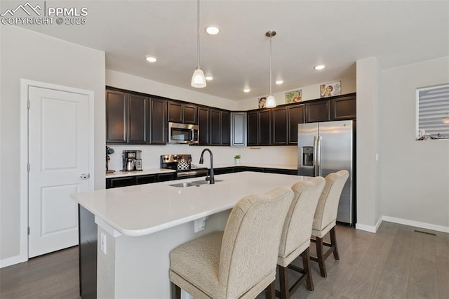 kitchen with appliances with stainless steel finishes, decorative light fixtures, sink, a kitchen island with sink, and dark brown cabinets