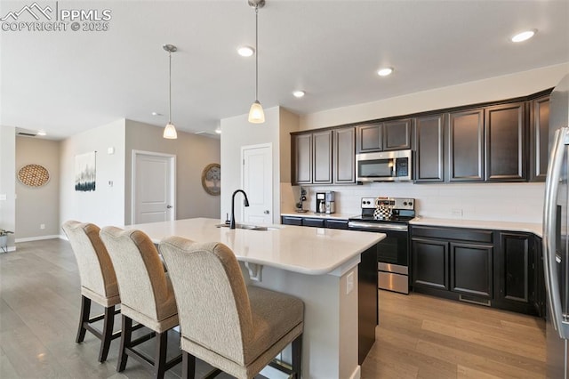 kitchen with sink, hanging light fixtures, an island with sink, stainless steel appliances, and decorative backsplash