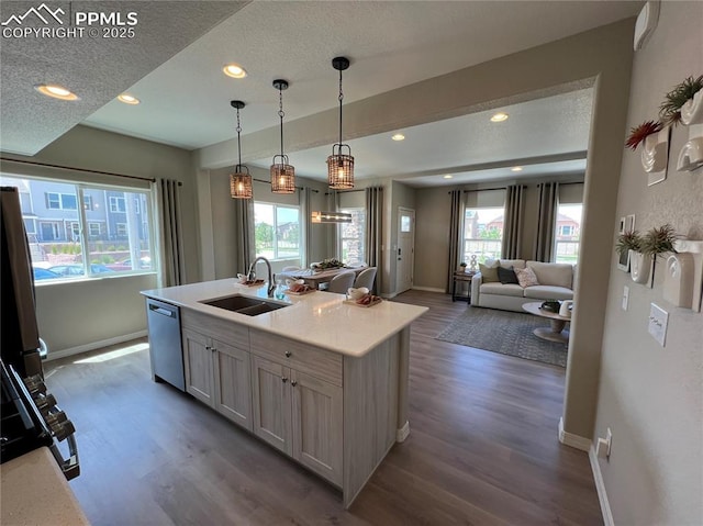 kitchen with dark wood-type flooring, sink, decorative light fixtures, a center island with sink, and appliances with stainless steel finishes