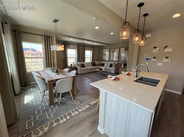 kitchen with pendant lighting, sink, dark hardwood / wood-style flooring, light stone counters, and a center island with sink