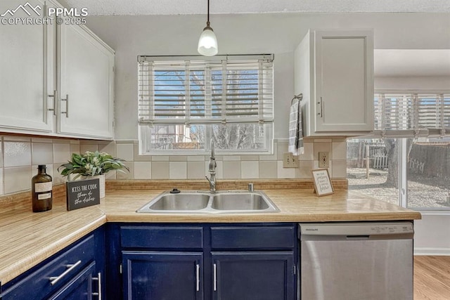 kitchen featuring tasteful backsplash, light countertops, a sink, blue cabinets, and dishwasher