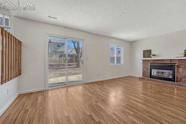 unfurnished living room featuring baseboards, a fireplace, visible vents, and wood finished floors