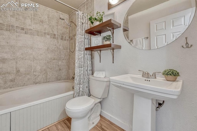 full bathroom featuring a textured wall, toilet, shower / bath combo with shower curtain, wood finished floors, and baseboards