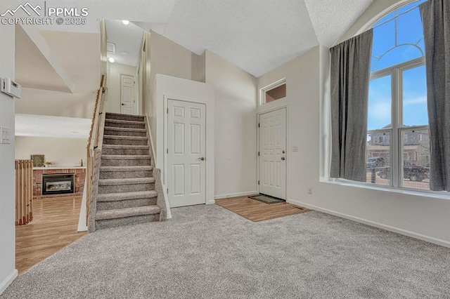 entryway featuring baseboards, carpet, stairs, vaulted ceiling, and a brick fireplace