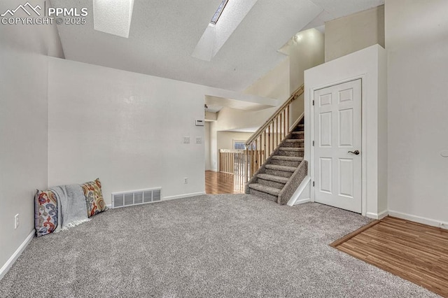 interior space with vaulted ceiling with skylight, visible vents, baseboards, carpet, and stairs