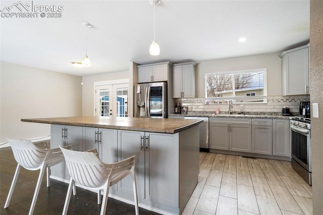 kitchen featuring wood counters, sink, hanging light fixtures, a center island, and stainless steel appliances