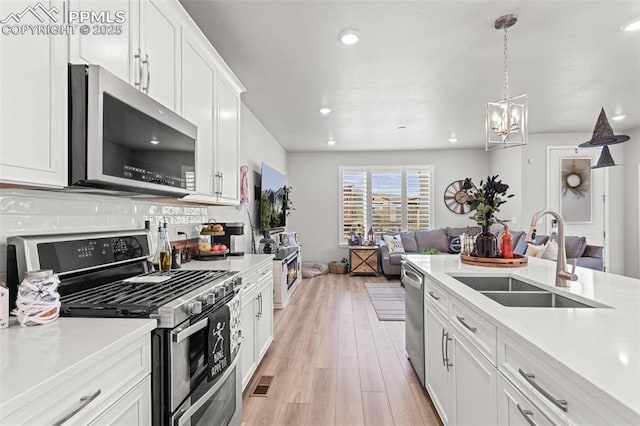 kitchen featuring sink, hanging light fixtures, stainless steel appliances, white cabinets, and light wood-type flooring