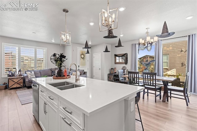 kitchen featuring pendant lighting, white cabinetry, sink, a kitchen island with sink, and a notable chandelier