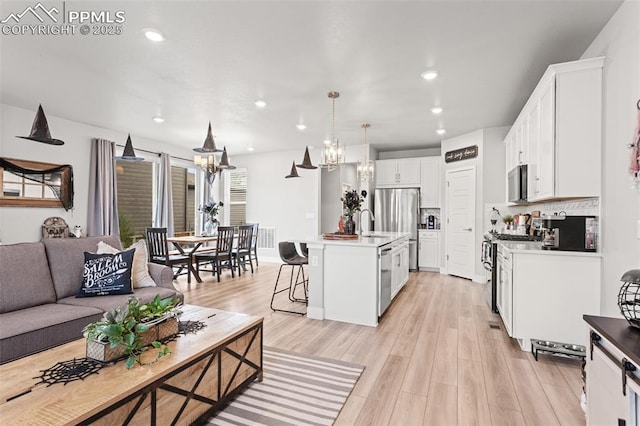 kitchen with hanging light fixtures, an island with sink, stainless steel appliances, light hardwood / wood-style floors, and white cabinets