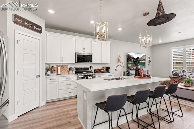 kitchen with sink, white cabinetry, decorative light fixtures, appliances with stainless steel finishes, and a kitchen island with sink