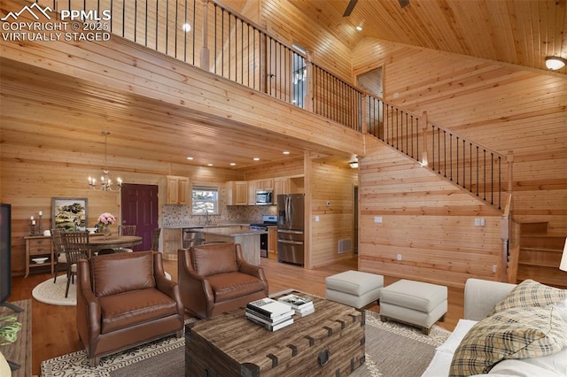 living room with wooden walls, high vaulted ceiling, ceiling fan with notable chandelier, wooden ceiling, and light wood-type flooring