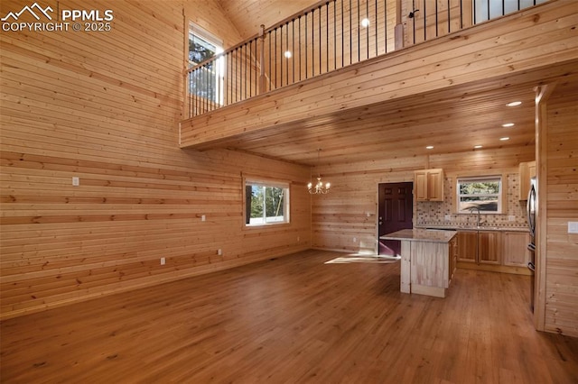 unfurnished living room featuring sink, an inviting chandelier, a towering ceiling, light hardwood / wood-style floors, and wood walls