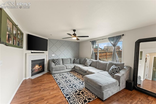 living room with ceiling fan, wood-type flooring, and a fireplace