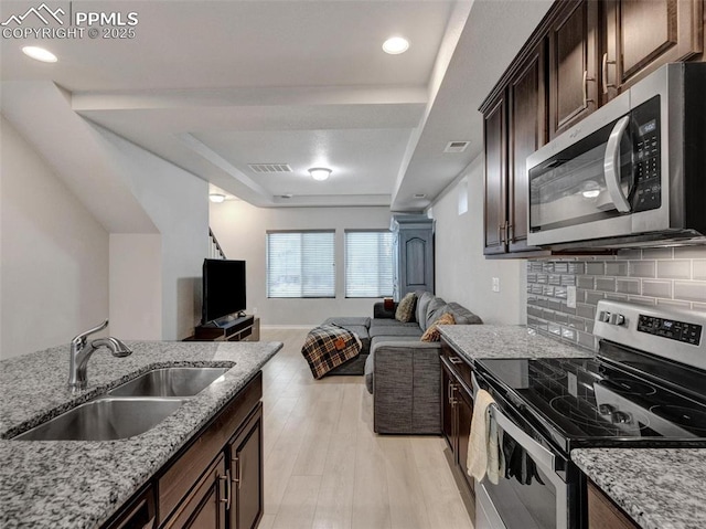 kitchen with sink, stainless steel appliances, light stone counters, tasteful backsplash, and a tray ceiling