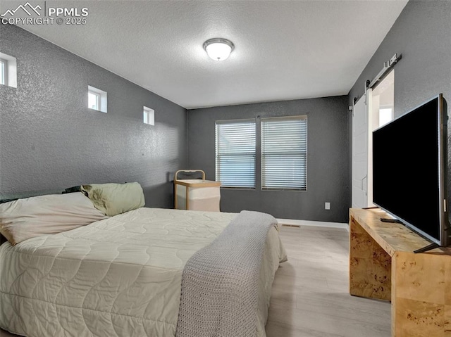 bedroom featuring a barn door, a textured ceiling, and light wood-type flooring