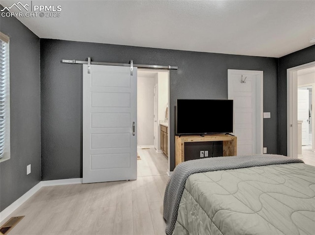 bedroom featuring ensuite bath, a barn door, and light wood-type flooring