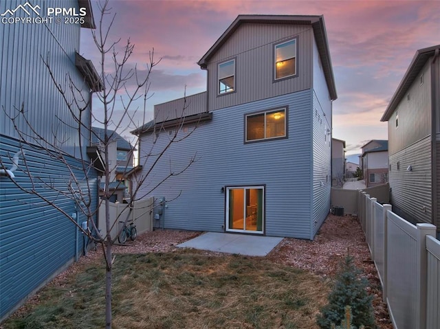 back house at dusk with a yard, central AC, and a patio