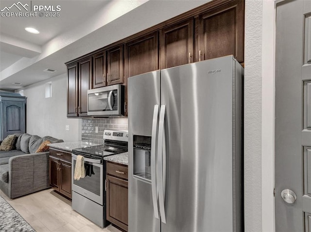 kitchen featuring tasteful backsplash, appliances with stainless steel finishes, light stone countertops, and dark brown cabinets