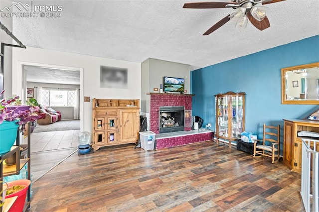 living room featuring ceiling fan, wood-type flooring, a brick fireplace, and a textured ceiling