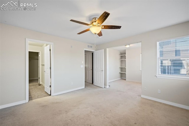 unfurnished bedroom with a walk in closet, light colored carpet, a closet, and ceiling fan