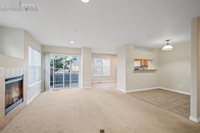 unfurnished living room featuring a tile fireplace, carpet floors, and a healthy amount of sunlight