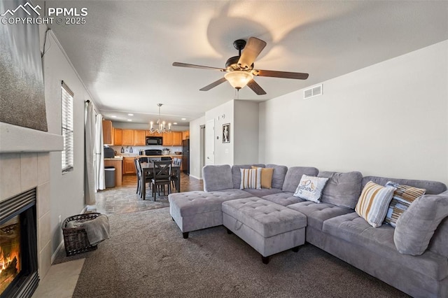 living room with light colored carpet, a tiled fireplace, and ceiling fan with notable chandelier