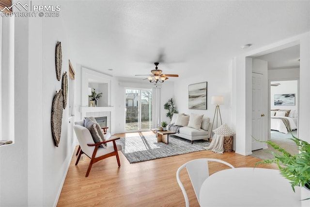 living room featuring ceiling fan, a tiled fireplace, and light hardwood / wood-style flooring