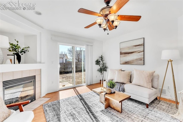 living room featuring a fireplace, ceiling fan, and light wood-type flooring