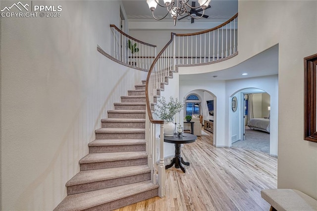 stairway with an inviting chandelier, wood-type flooring, and a high ceiling